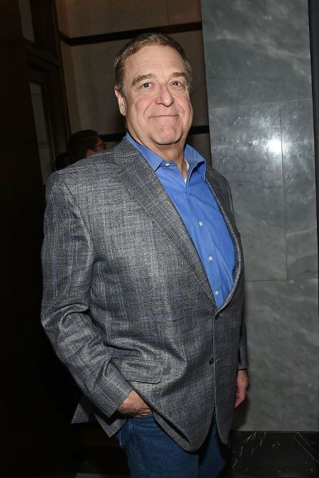 John Goodman in a grey blazer and blue shirt poses for a picture.